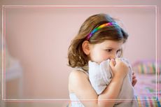 An unhappy looking girl holding a comfort blanket to her face