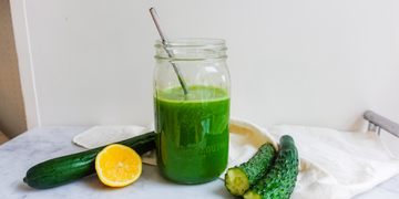 a glass of green liquid with limes and a lemon slice on a table