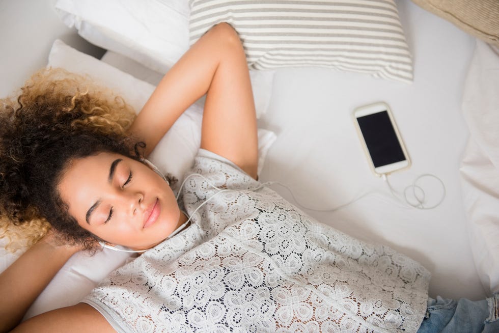 mixed race woman laying on bed listening to music on cell phone