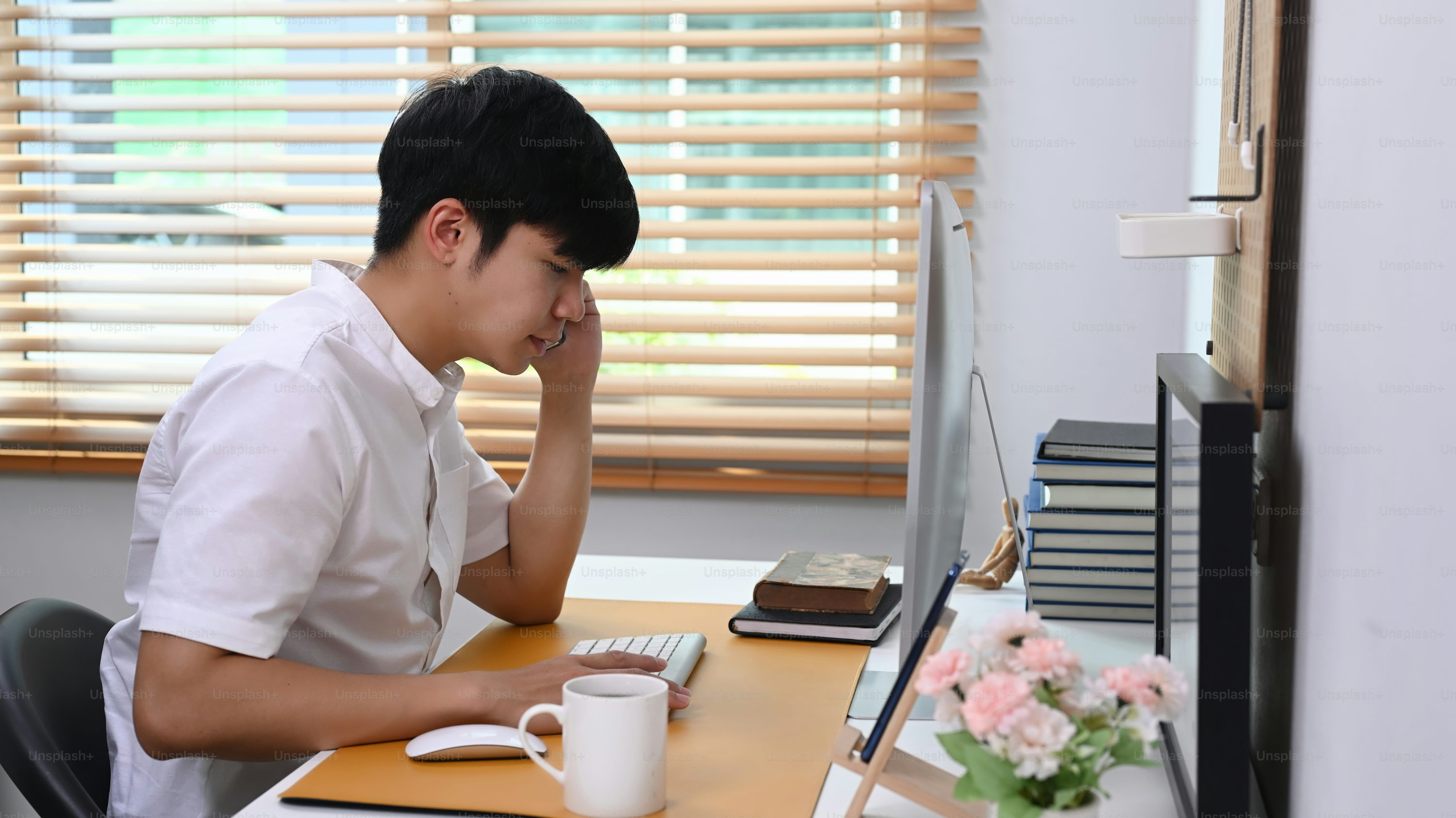 Side view of young man talking on mobile phone while sitting at comfortable home office.