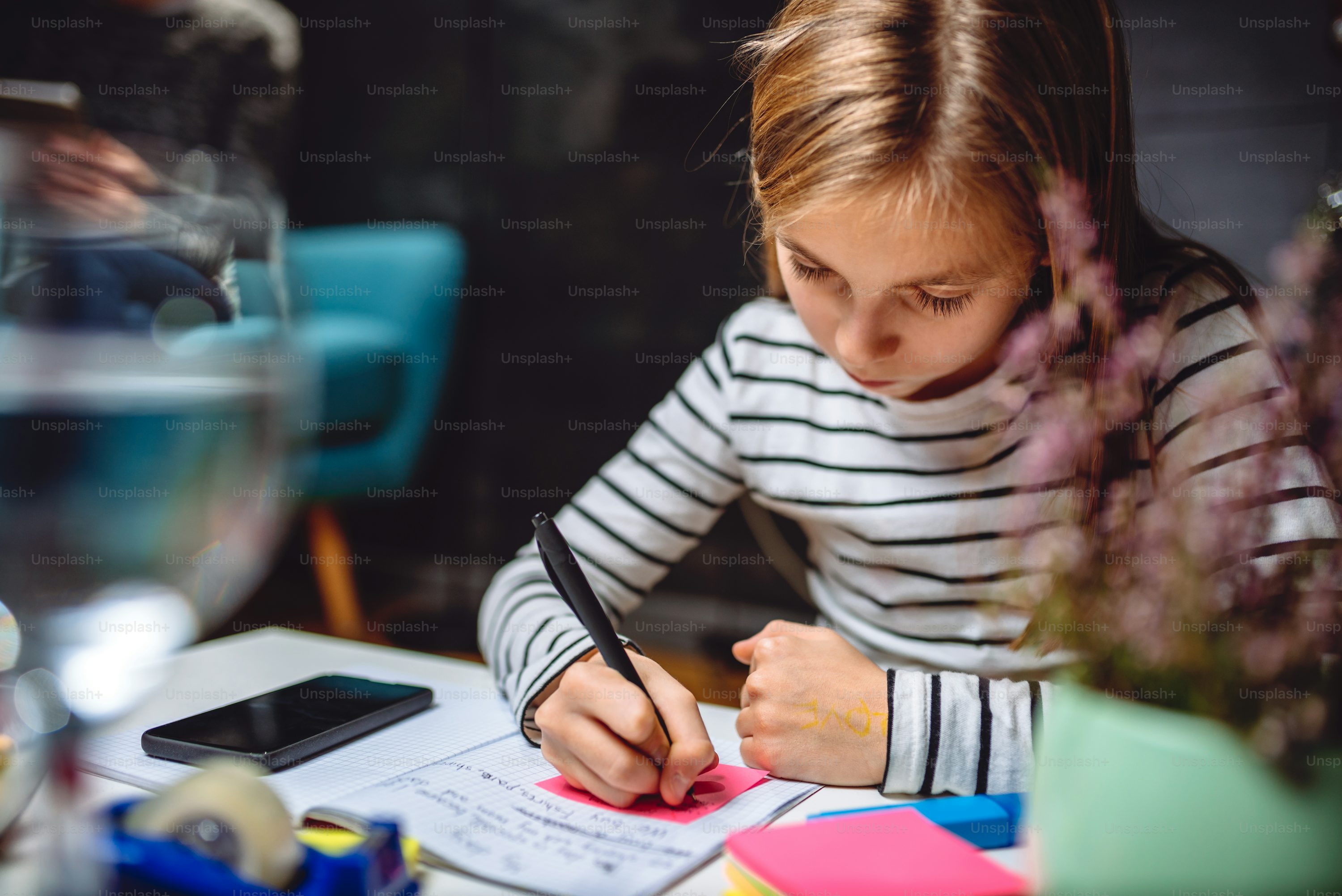 Girl sitting at coffee table in living room with her mother in the background and doing homework late at night