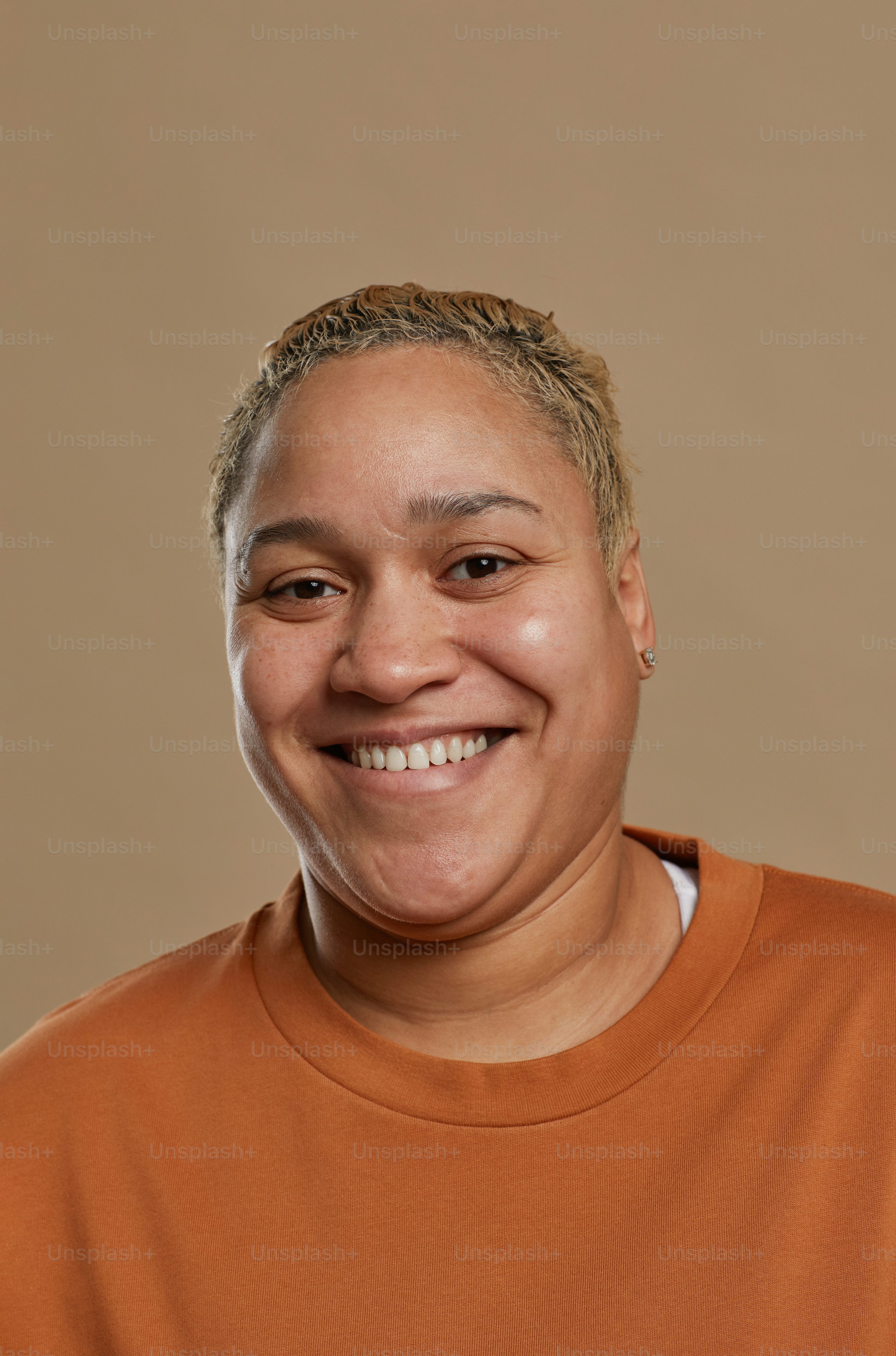 Vertical portrait of short haired mixed race woman looking at camera and smiling happily while posing against neutral background in studio