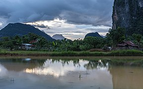 Water reflection of karst mountains, wooden houses and trees in a paddy field at sunset in Vang Vieng Laos.jpg