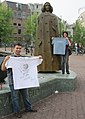 2009-06-27 #00400 Young couple at Baruch de Spinoza statue between Stopera and Zwanenburgwal in Amsterdam presents the blue and the white Free Travel-Shirt