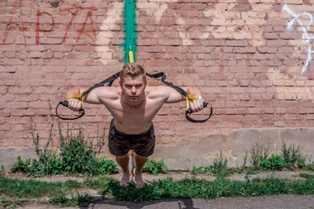 Male athlete is an excellent training wringing out in nature in the city in summer training trx feel your strength and balance motivation tanned skin exercise pectoral muscles a sunny day