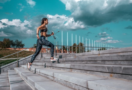 Young athletic girl running morning for jog fitness training sportswear leggings and top phone listens music headphones summer city workout online playlist application to internet free space