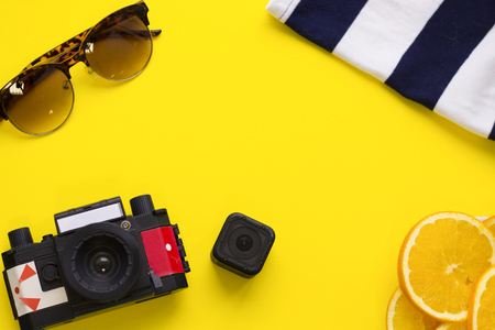 Beach concept background cameras and beach outfit on a bright yellow background top view space for a text or product display