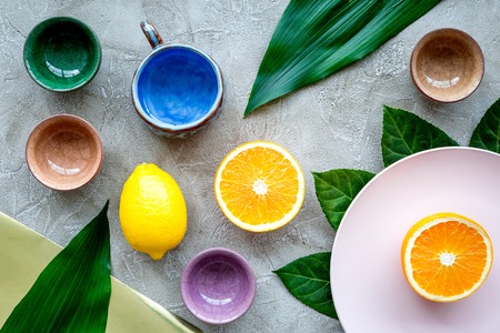 Tableware pattern cups and plates decorated by exotic leaves and fruits on grey background top view