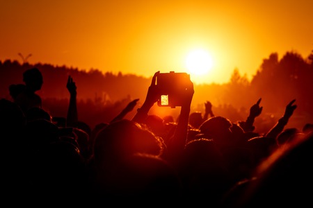 Shooting on a mobile phone during the summer music festival black silhouette of raised hands sunset