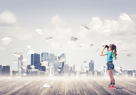 Cute kid girl stand on wooden floor and paper planes flying around Stock Photo