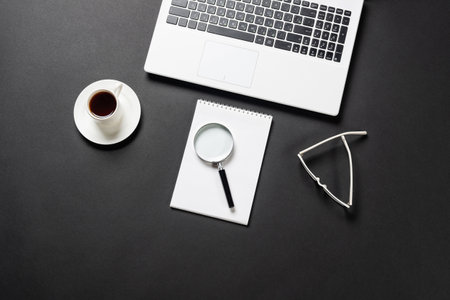 Still life of office workplace with cup of coffee and copy space flat lay black surface with laptop and magnifier on notebook consulting audit and accounting top view modern office workspace