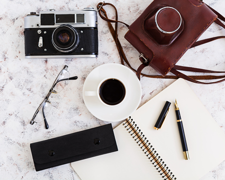 Flat lay top view office table desk desk workspace with retro camera diary pen glasses case cup of coffee on white background