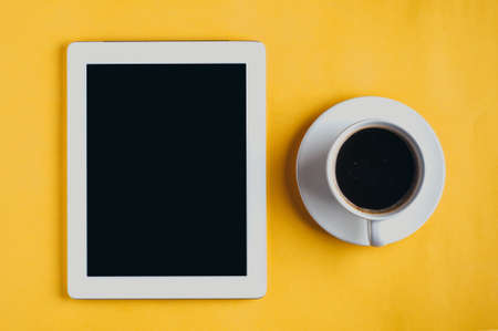 Tablet pc and coffee cup on yellow background Stock Photo