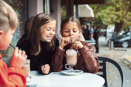 Los niños se divierten en el café al aire libre. Niños hablando y bebiendo cacao para el desayuno en la calle de la ciudad en otoño. Pasar el fin de semana con amigos. Foto de archivo