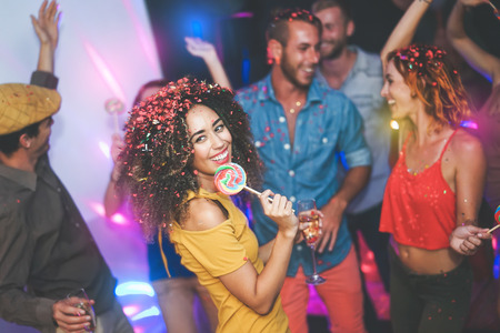 Group of friends dancing and drinking champagne at nightclub young happy people having fun and enjoying party eating candy lollipops youth friendship lifestyle concept Stock Photo