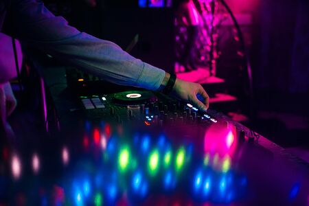 Hands dj mixing and playing music on a professional controller mixer in a nightclub