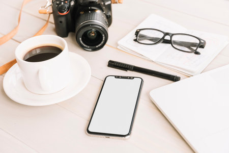 Smartphone with blank screen coffee cup camera and notebook on wooden table