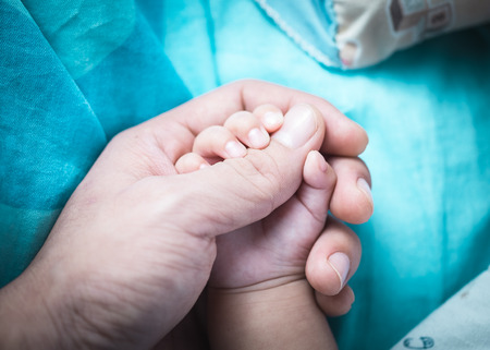 Holding hands hand the sleeping baby in the hand of parent close up