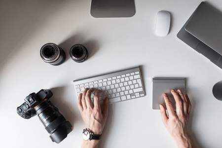 Designer is sitting at workplace and typing on the keyboard top view of men s hands and on a table with a photo camera with lenses for camera with a graphic tablet with a mouse photographer works