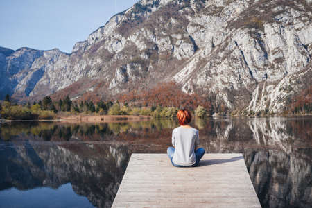 Jovem mulher está sentada na ponte de madeira de bela natureza ao redor do lago Bohinj na Eslovênia. O Parque Nacional Triglav, Julian Alps, Eslovênia.