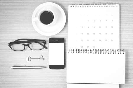 Coffee and phone with key eyeglasses notepad calendar on wood table background black and white color Stock Photo