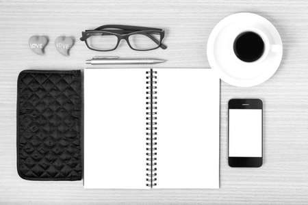 Office desk coffee with phone notepad eyeglasses wallet heart on wood background black and white color