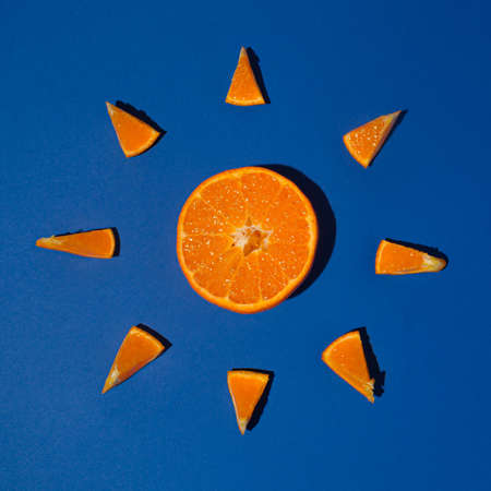 Fresh fruit juicy orange tangerin in the shape of the summer sun organic fruit and many slice on the royal blue background flat lay