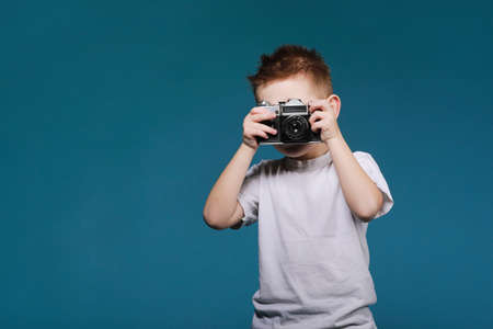 Little boy taking a picture using a retro camera child boy with vintage photo camera isolated on blue background old technology concept with copy space child learning photography Stock Photo