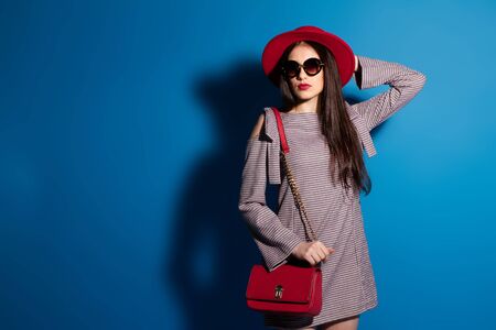 Lovely model in fashionable red hat and a red clutch on blue background Stock Photo