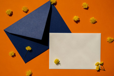 Beautiful little yellow chamomile daisies flowers on postal blue envelope on orange background empty paper note copy space for text spring time greeting card for holiday minimalism concept vivid colors creative delicate yellow flowers