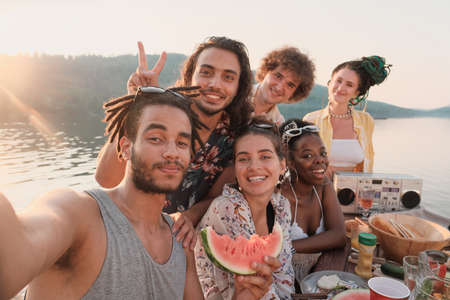 Retrato de un feliz grupo de amigos sonriendo y posando ante la cámara mientras hacen un retrato selfie durante un picnic al aire libre