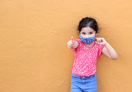 Niña latina de 6 años con máscaras protectoras covid 19 con pared de color de fondo nueva normalidad