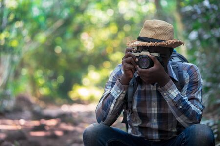 African freedom man traveler holding camera with backpack standing in the green natural forest Stock Photo