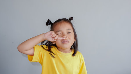 Imagen de un niño asiático con camiseta amarilla estornuda sobre fondo gris.