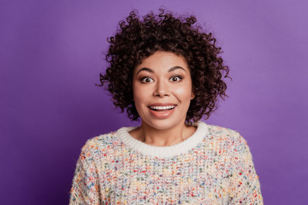 Cara de mujer joven feliz sorprendida con emoción mira la cámara en la pared púrpura