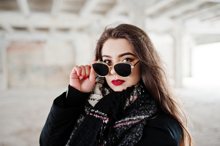 Brunette stylish casual girl in scarf and sunglasses against abandoned factory place