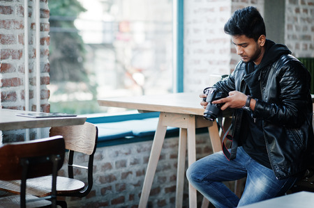 Smart young asian man photographer wear on leather jacket spending time at cafe and looking at his camera