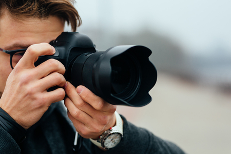 Detail view of young man in eyeglasses taking photos on the street dressed in warm jacket fashinable white watches