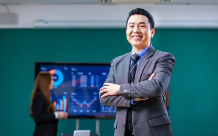 Portrait shot millennial asian professional successful male businessman ceo entrepreneur in formal business suit standing crossed arms smiling meeting room with male and female colleagues discussing Stock Photo