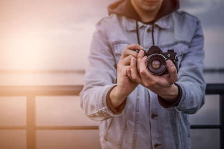 A man in a denim jacket with a vintage film camera at sunset