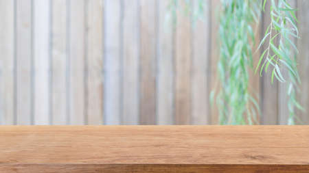 Mesa de madera vacía y pared de madera borrosa en el fondo del jardín con hojas verdes - se puede utilizar para mostrar o montar sus productos. Foto de archivo