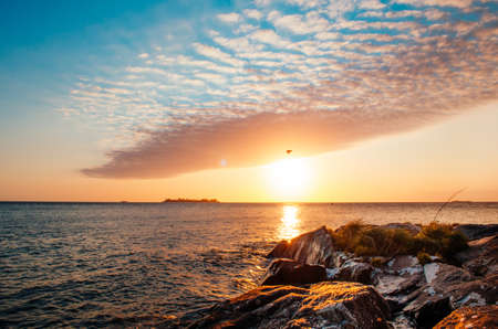 Una captura sin aliento de la hora dorada en Colonia Del Sacramento, Uruguay con vista al Río De La Plata y un solo pájaro volando sobre las nubes.