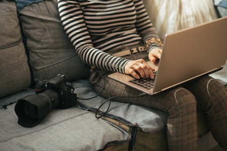 Closeup on young woman with modern dslr photo camera using laptop in loft apartment Stock Photo