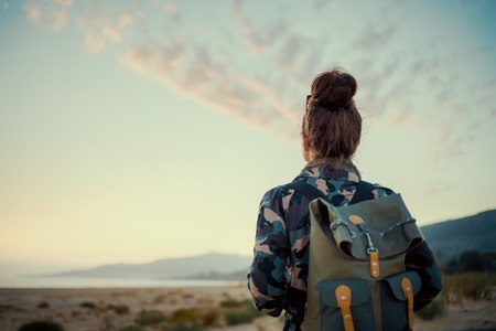 Seen from behind active tourist woman in hiking clothes against mountain and sea landscape at sunset Stock Photo