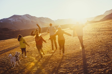 Gran grupo de amigos felices corren y saltan en el campo al atardecer contra las montañas y el sol