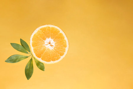 Fresh orange slice with green leaves on a yellow background top view close up copy space