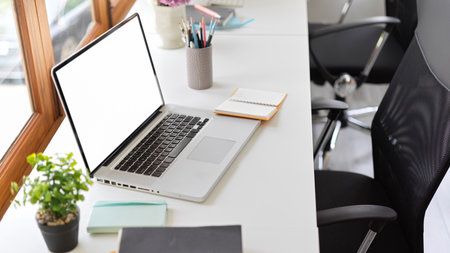 Close up office desk with open portable laptop computer white screen mockup and office supplies