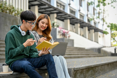 Happy and smiling young asian college students are talking sharing ideas scrolling on a textbook working on their school project together in front of the campus building