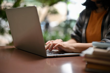 Cropped image of a young asian woman in casual clothes using her laptop computer at an outdoor cafe