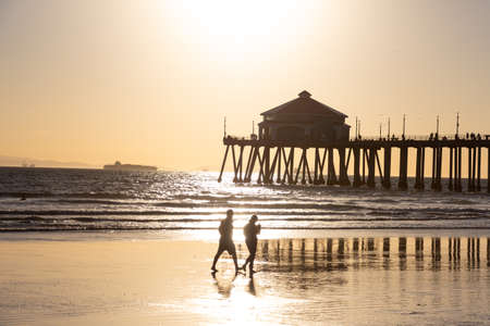 Una pareja caminando por la playa frente al muelle en Huntington Beach, California al atardecer Foto de archivo